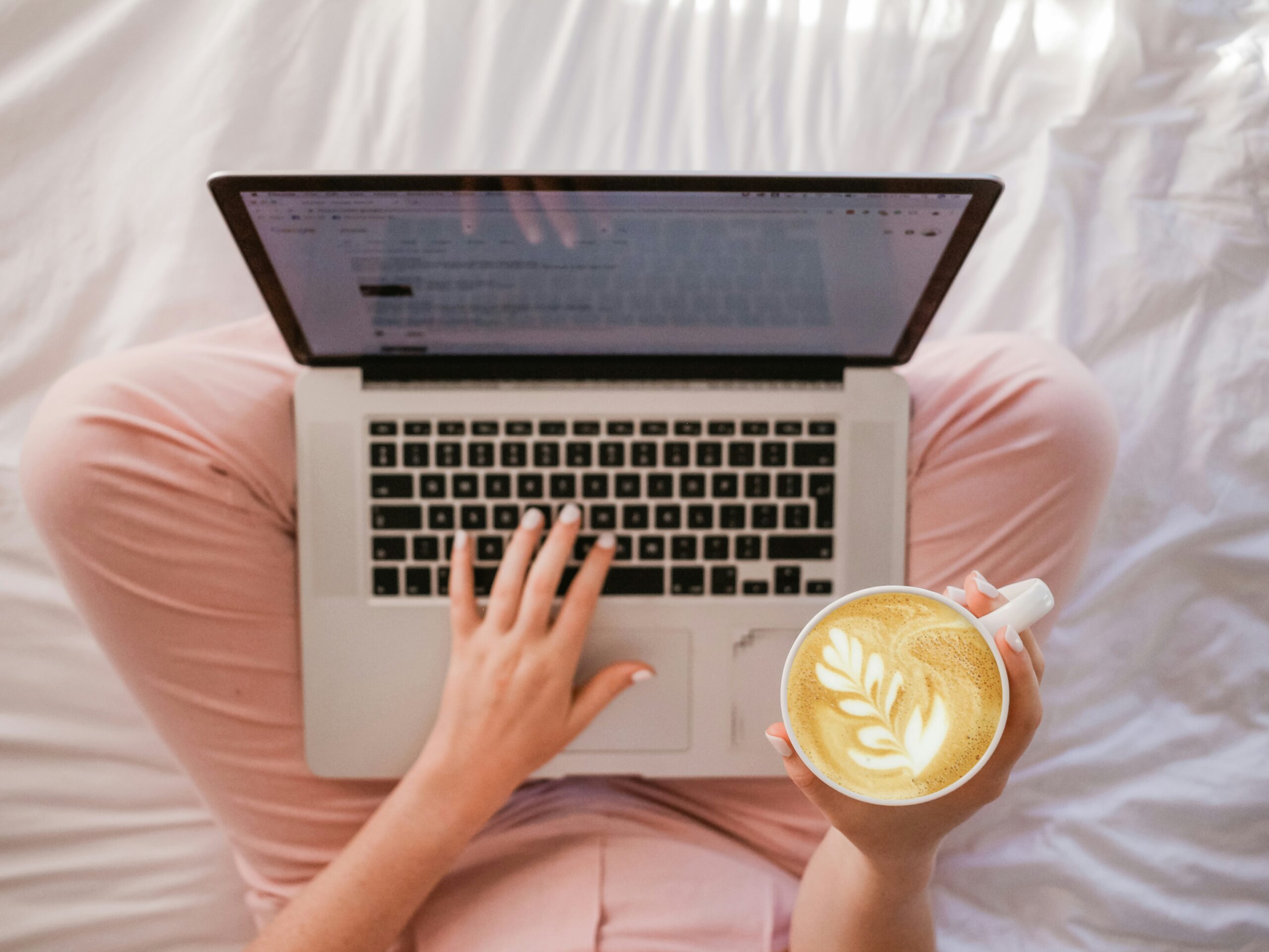 business to start with no money. woman in pink pants holding a cappucino with a laptop on her crossed legs